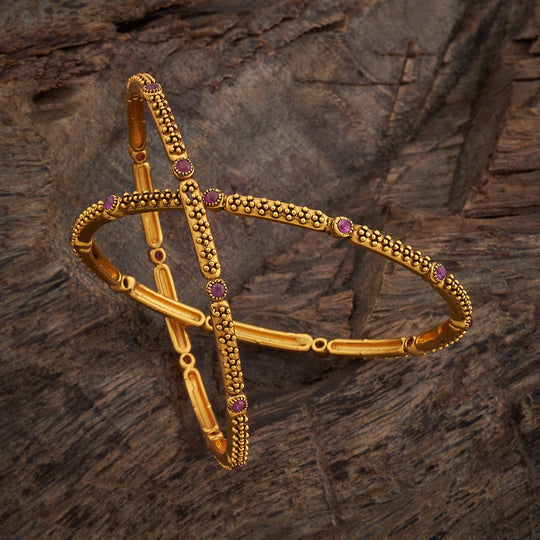 Antique gold polish bangles with ruby round stones on wooden surface.