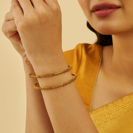 Antique gold bangles with ruby stones worn by a model in yellow attire.