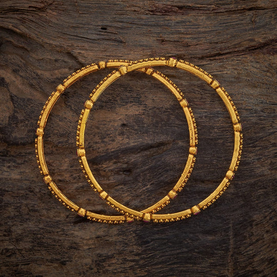 Pair of antique gold bangles with ruby stones on textured wood.