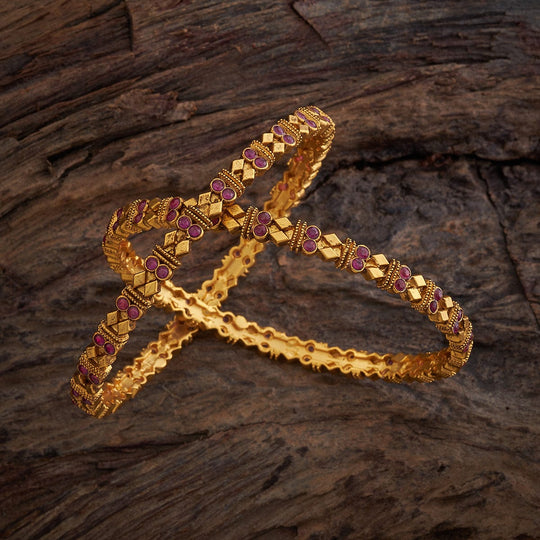Antique gold polish bangles with ruby round stones on a wooden surface.