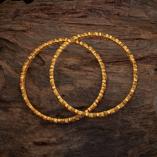 Pair of thin antique gold-tone bangles with subtle ruby accents on wood.
