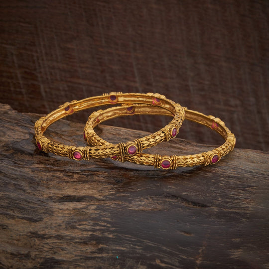Pair of antique gold polish bangles with ruby stones on dark wood.