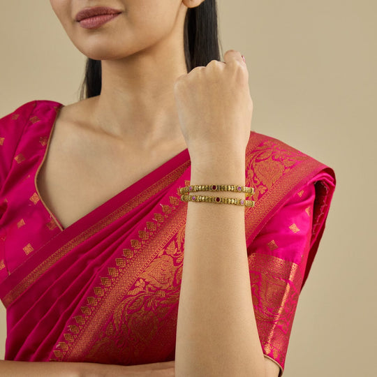 Model wearing antique gold polish bangles with ruby stones on wrist.
