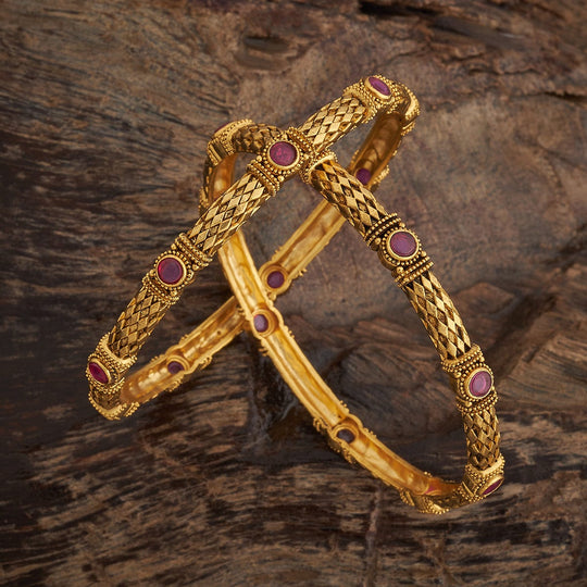 Antique gold polish bangles with ruby round stones on wooden surface.
