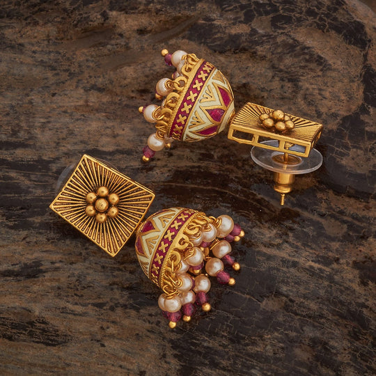 Close-up of antique temple jhumka earrings with ruby-red stones and pearl drops.