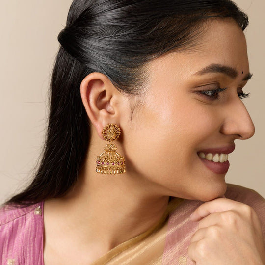Model wearing antique jhumka earrings with peacock motif and ruby-red stones.