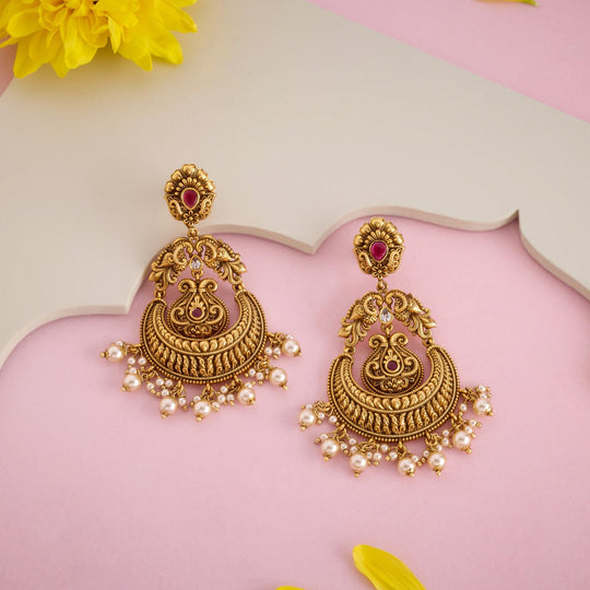 Antique temple earrings with ruby-red stones and pearl drops, on a pink surface.