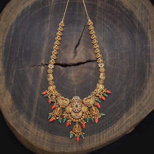 Long antique necklace with peacock design on wooden stand, red and green drops.