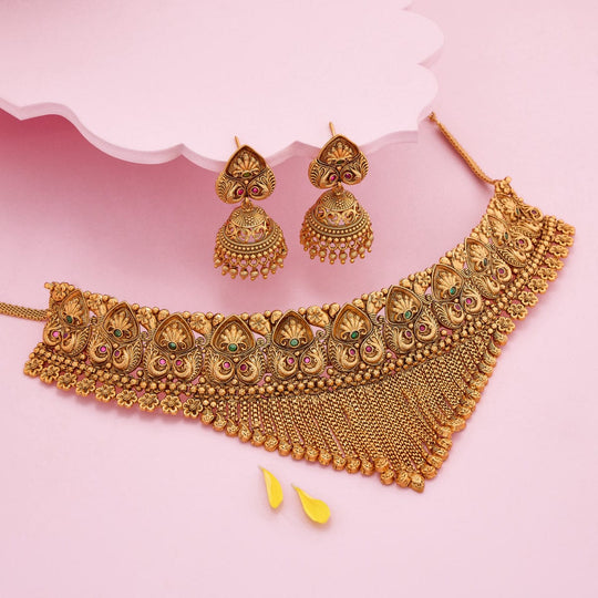 Antique necklace and earrings set with peacock motif on a pink background.