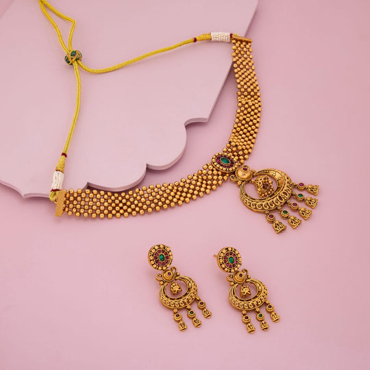 Antique necklace set with earrings on a pink surface, showing intricate details.