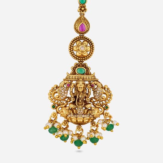 Close-up of antique tikka with deity motif, green and pink stones.