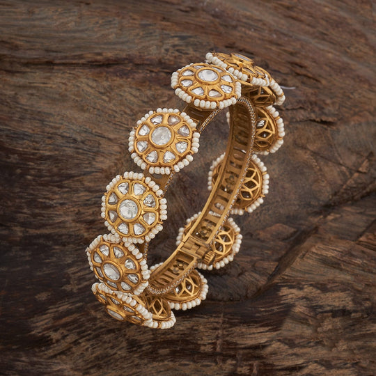 Antique floral Kundan bangle with white stones on wooden surface.
