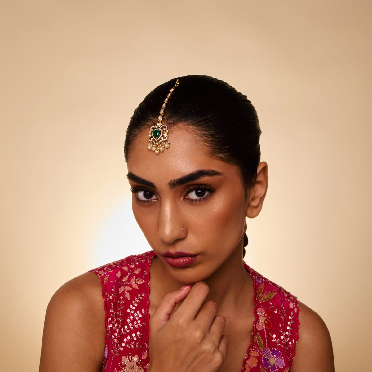 Model wearing kundan tikka with green stone and pearl accents.