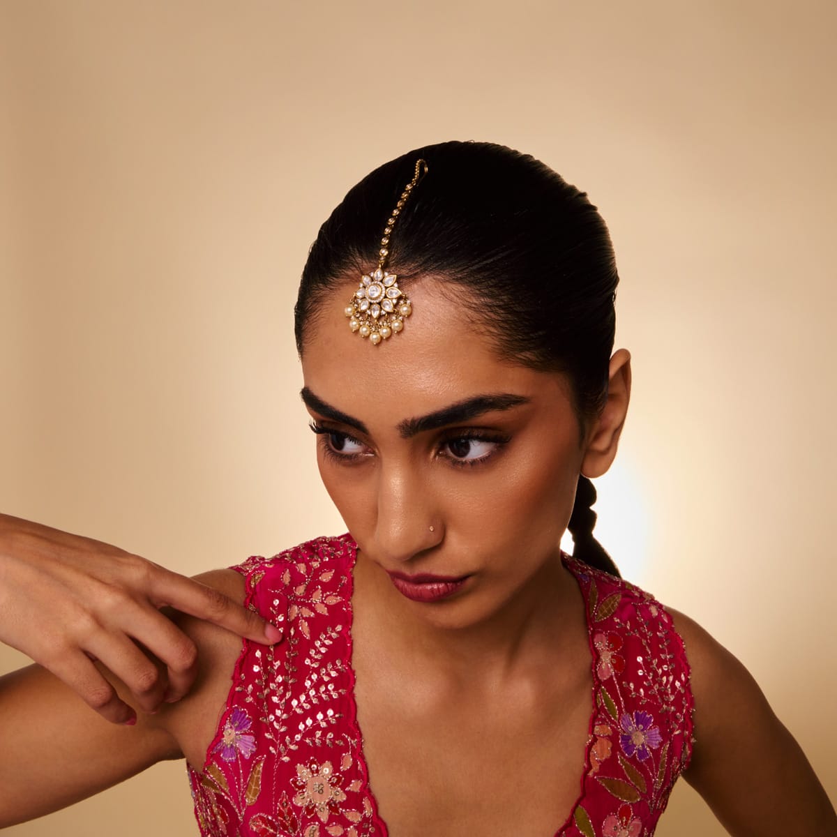 Model wearing a Kundan tikka with white stones and pearl drops.