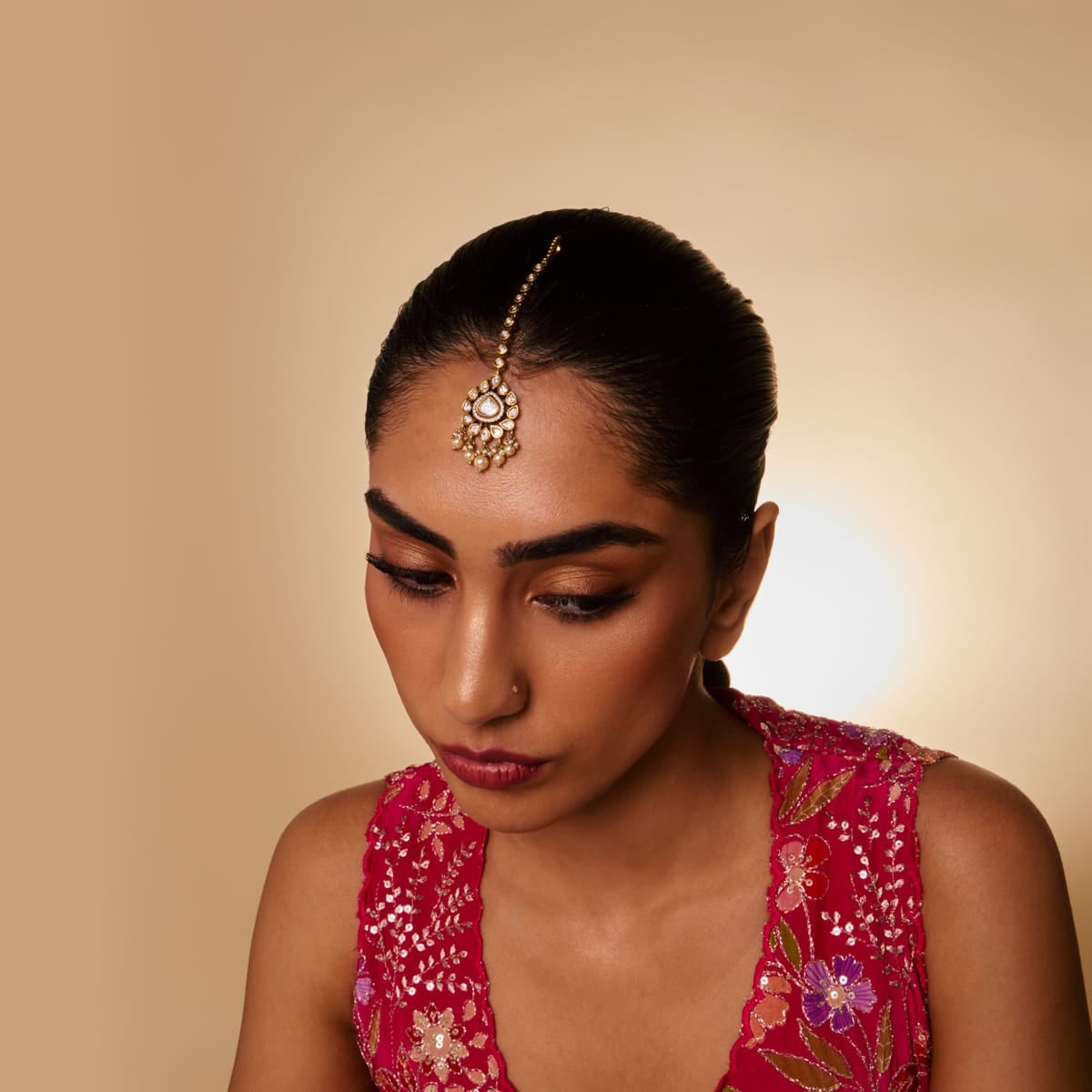 Model wearing a kundan tikka with white stones and pearl drops.
