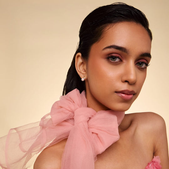 Model wearing gold-tone stud earrings with pearl and zircon stones.