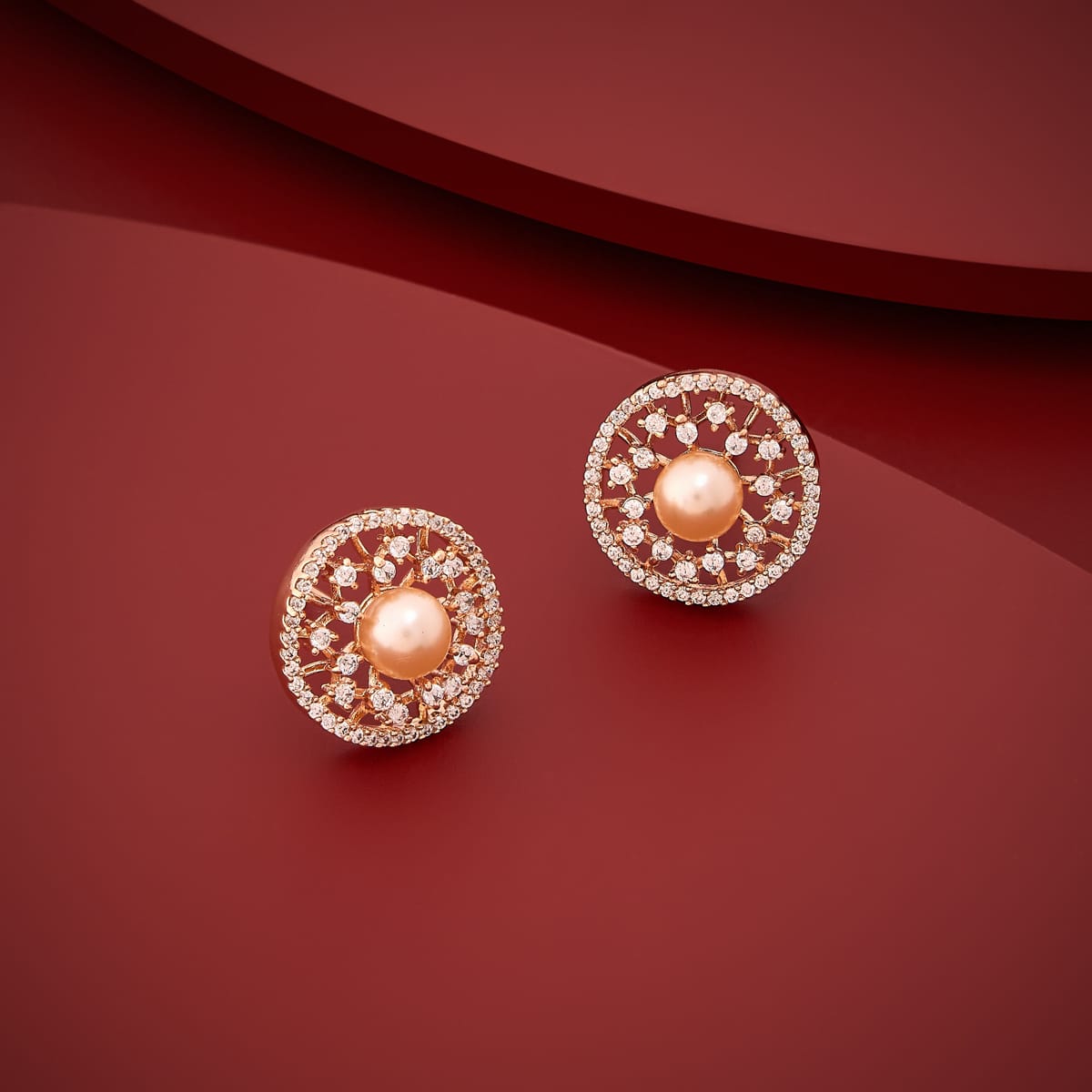 Gold-tone zircon and pearl stud earrings on red background, angled view.
