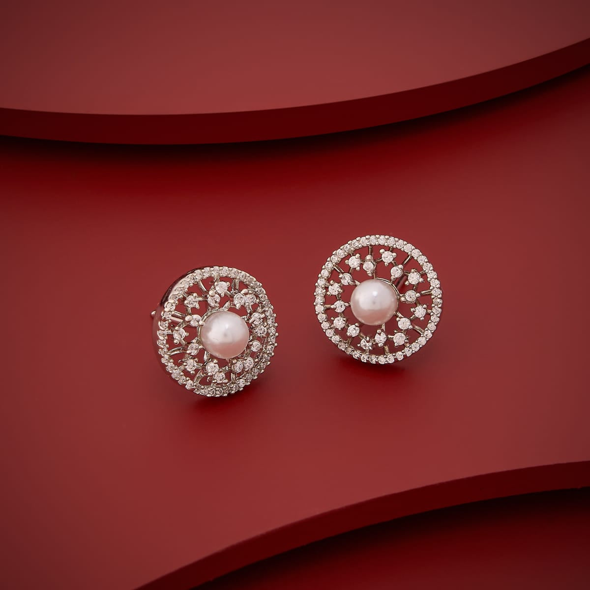 White zircon and pearl stud earrings on red background, angled view.