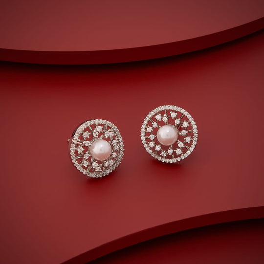 White zircon and pearl stud earrings on red background, angled view.