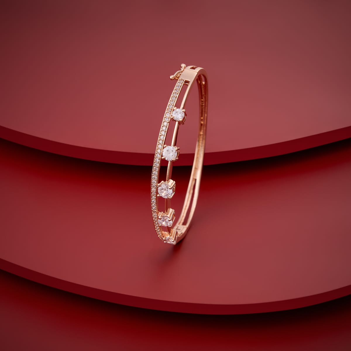 Gold-tone zircon kada with white stones, angled view on red background.