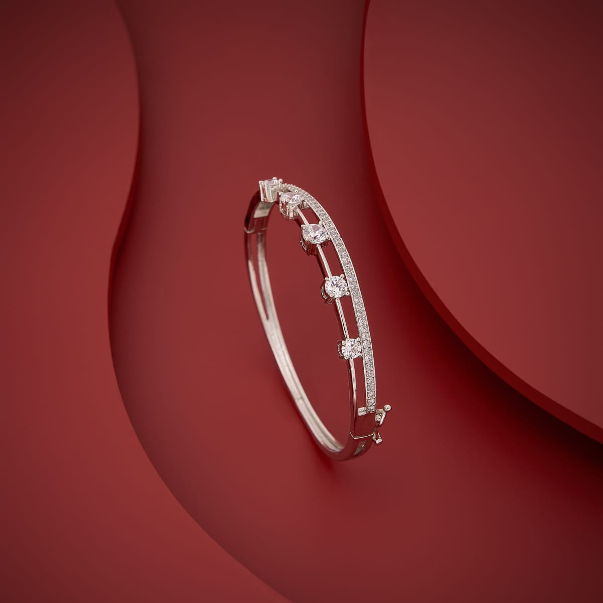 Silver-tone zircon kada with white stones, angled view on red background.