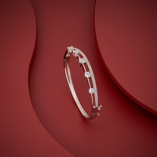 Silver-tone zircon kada with white stones, angled view on red background.