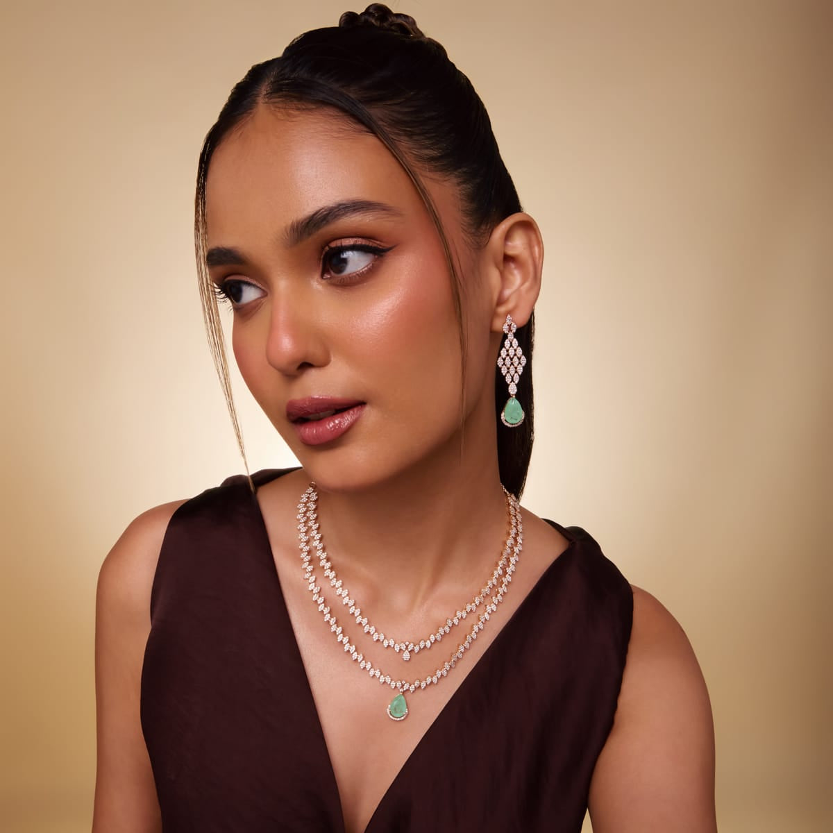 Model wearing layered zircon necklace and earrings with green teardrop stones.