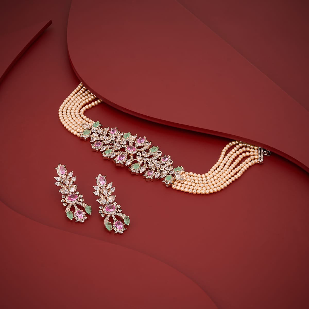 Zircon necklace set with pink and green stones and pearls on red background.