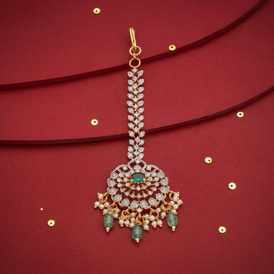 Floral zircon tikka with green drops, gold polish, on red background with sequins.