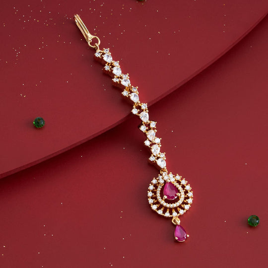 Gold polish zircon tikka with ruby-red stones, laid on red surface, angled view.